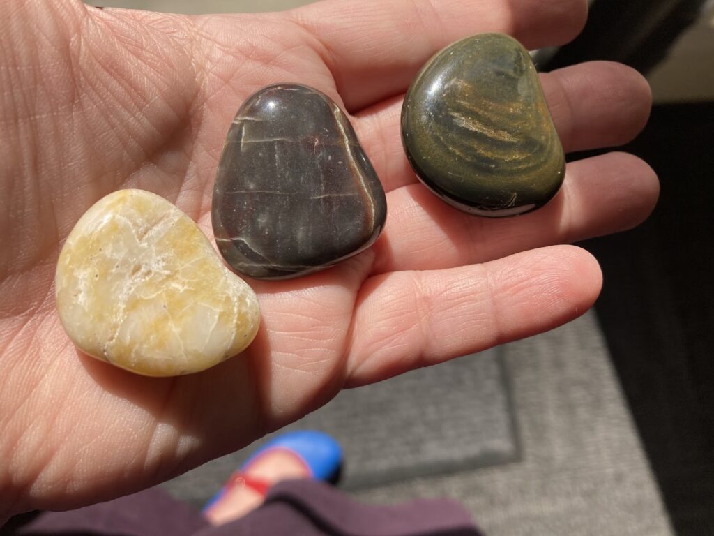 hand holding three small smooth rocks, with varied coloration