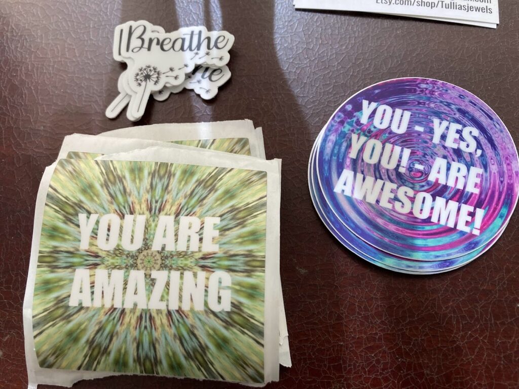 three piles of stickers on a table. "Breathe", "You are amazing," and "You - yes you - are awesome!"
